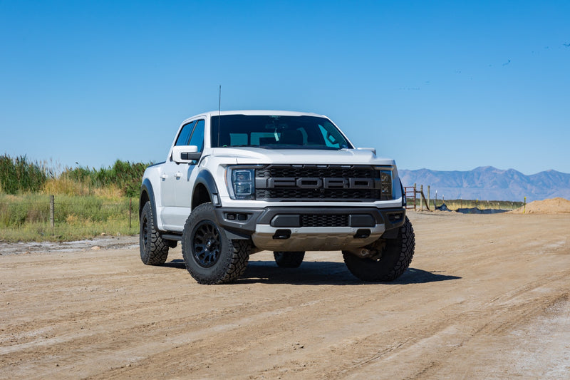ReadyLIFT Leveling Kit installed on a Ford F-150 Raptor: white Ford F-150 Raptor crew cab on black wheels on a dirt road with mountains behind