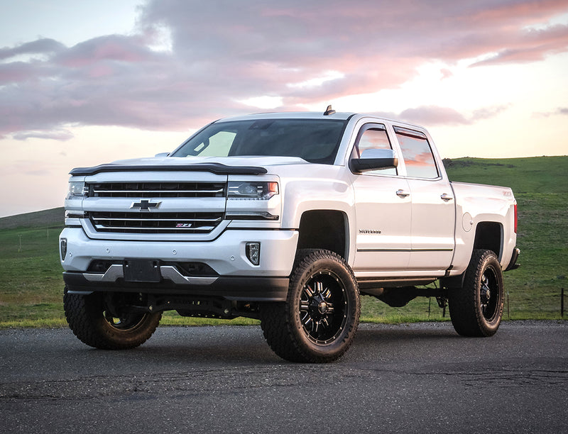 ReadyLIFT Lift Kit installed on a Chevrolet Silverado 1500: white Chevrolet Silverado 1500 Z71 crew cab lifted on black wheels, low front angle on a road at sunset
