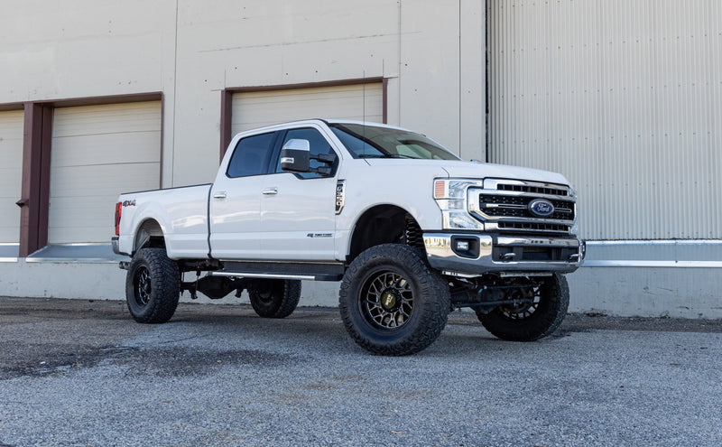 ReadyLIFT Lift Kit installed on a Ford F-250 Super Duty: white Ford Super Duty crew cab long bed lifted on bronze wheels in front of a warehouse