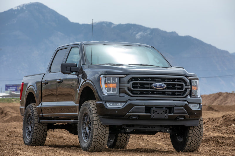 ReadyLIFT MAX3.3 Suspension System installed on a Ford F-150: black Ford F-150 crew cab lifted on bronze wheels on a dirt lot with mountains behind