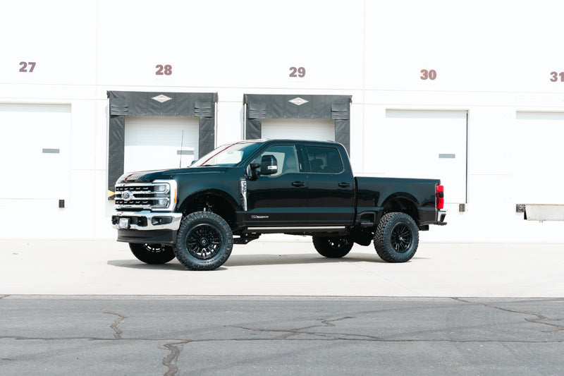 ReadyLIFT SST Lift Kit installed on a Ford F-250 Super Duty: A black lifted Ford Super Duty Crew Cab parked in front of a white warehouse with loading doors