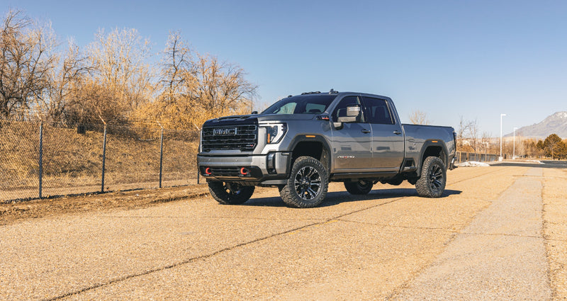 ReadyLIFT SST Lift Kit installed on a GMC Sierra 2500HD: A gray lifted GMC Sierra HD AT4 Crew Cab parked on a road with bare trees behind