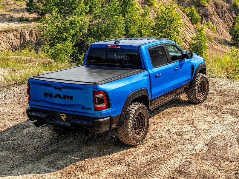 Retrax IX cover closed on a blue pickup parked on a dirt trail, rear three-quarter view