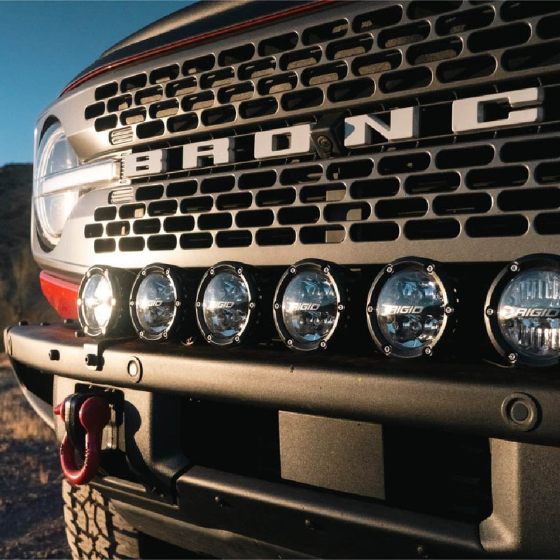 Rigid 360 Connect 30" Light Bar Assembly installed on a Ford Bronco: close low view of a row of round Rigid 360-Series pods on a bar across the front bumper of a Ford Bronco with BRONCO grille lettering