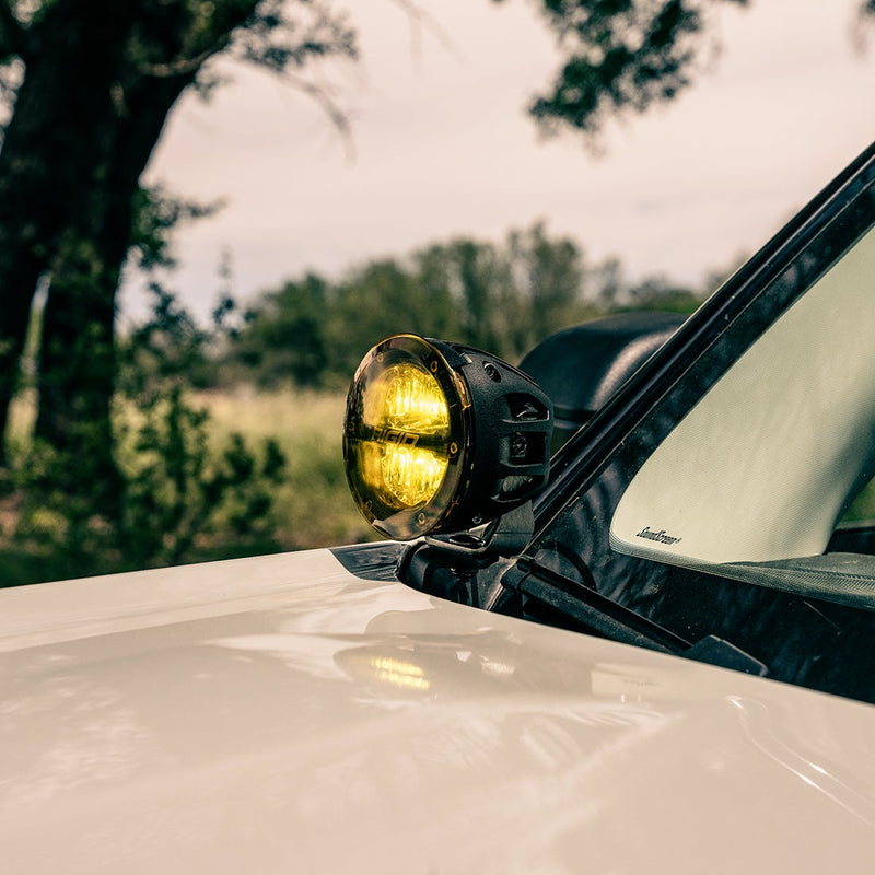 Rigid 360-Series 4" Drive A-Pillar Light Kit installed on a vehicle: round 4" pod with an amber cover mounted at the A-pillar of a white vehicle beside the windshield