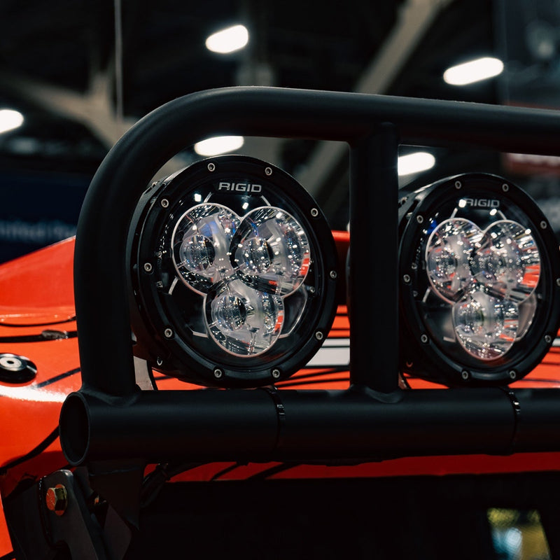 Rigid 360-Series Laser Optic 6" Amber PRO Pair installed on a vehicle: A pair of 6" Rigid 360-Series lights with clear three-optic faces mounted on a black tube bar of a red vehicle