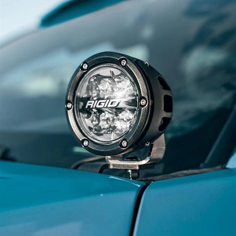Rigid 360-Series Spot A-Pillar Kit installed on a vehicle: close-up of a black round 360-Series spot light mounted on the A-pillar of a teal vehicle