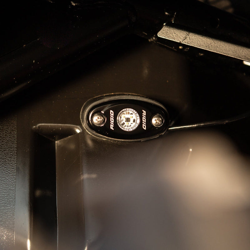 Close-up of the Rigid A-Series Low Power White: A black oval rock light mounted on the underside of a metal panel casts a soft white glow