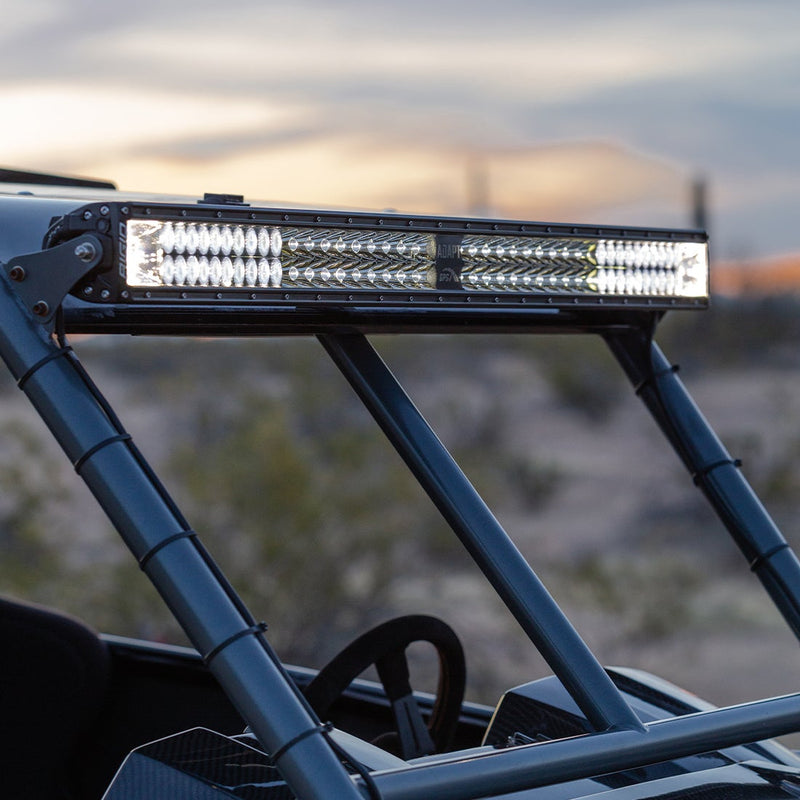 Rigid Adapt E-Series 30" installed on a vehicle: A lit Rigid Adapt E-Series light bar mounted across the top of a UTV roll cage in the desert at dusk