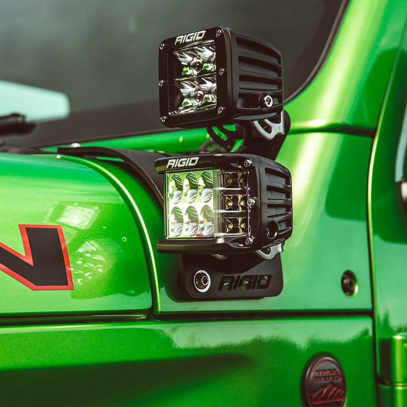 Rigid Cowl Mounts Short Standoff Mount Kit installed on a Jeep Wrangler JL: two Rigid D-Series pods sit on a cowl mount beside the windshield of a green Jeep, the lower pod lit