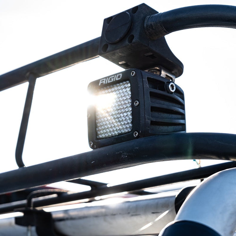 Close-up of the Rigid D-Series PRO Pods Pair: A D-Series PRO pod with a diffused lens glowing, clamped under a vehicle cage tube with sun behind