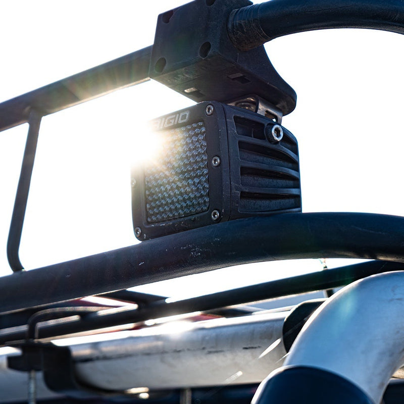 Close-up of the Rigid D-Series PRO Pods Pair: A D-Series PRO pod with a diffused lens shining, mounted on a cage tube against a bright sky