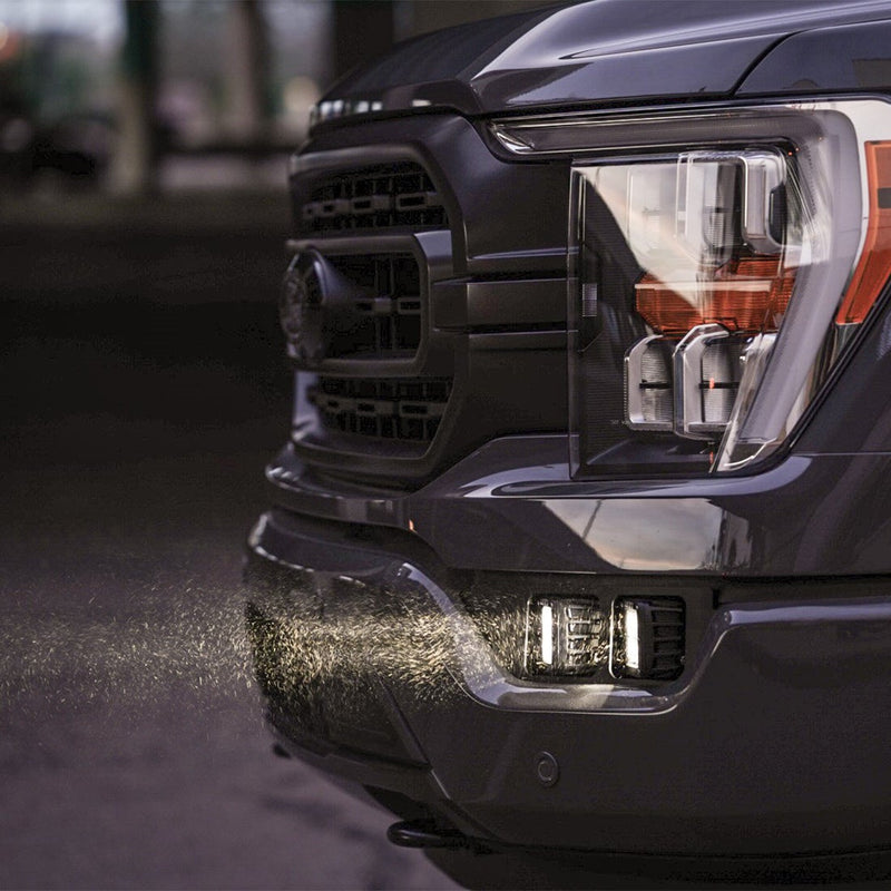 Rigid Dual Fog Mount installed on a Ford F-150: close-up of lit square pods in the fog pocket of a dark Ford F-150 with dust in the beam