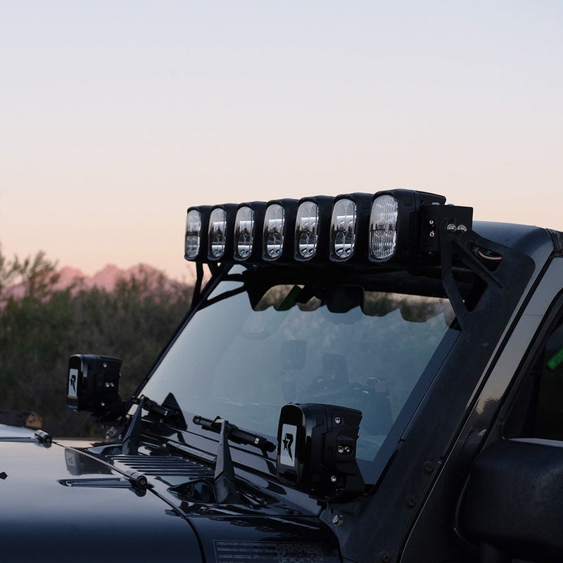 Rigid Phoenix 50" Connect Bar installed on a Jeep Wrangler: seven-pod connect bar mounted above the windshield of a black Jeep Wrangler with covered cowl pods