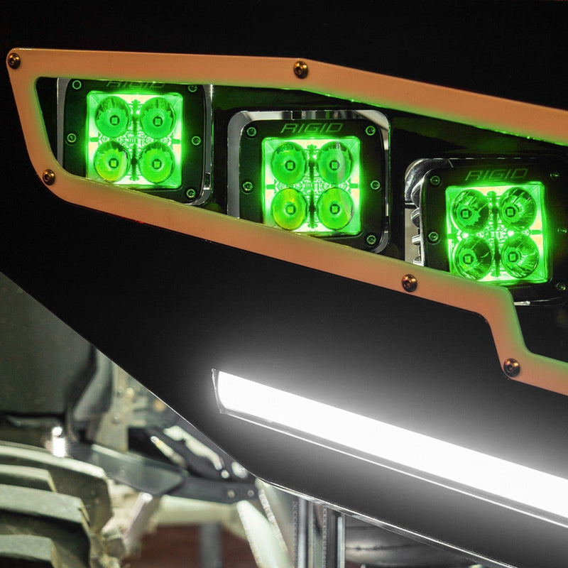 Rigid Radiance+ Pod RGBW Pair installed on a vehicle: three Radiance+ pods glowing green set into an orange-trimmed UTV bumper panel with a white light bar lit below