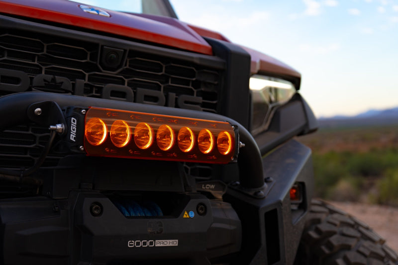 Rigid Revolve 10" Bar installed on a Polaris Polaris XPEDITION: A short Revolve light bar glowing amber on the front bumper of a Polaris side-by-side, with the POLARIS grille lettering above it