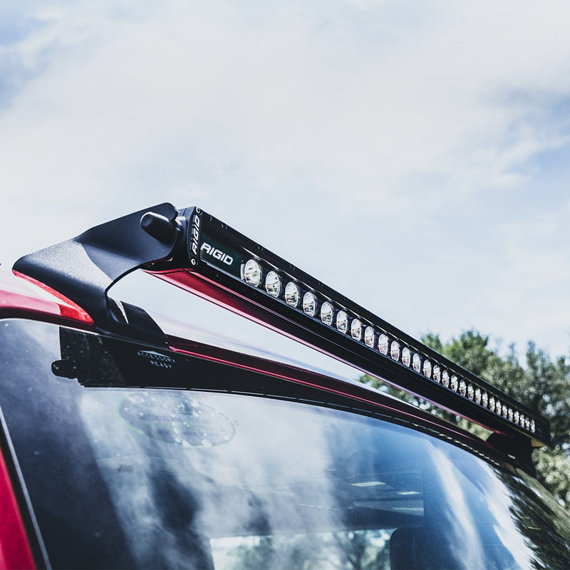 Rigid Roof Line Mount Kit for SR-Series installed on a vehicle: black SR-Series light bar held on roof-line mounts above the windshield of a red vehicle against a blue sky