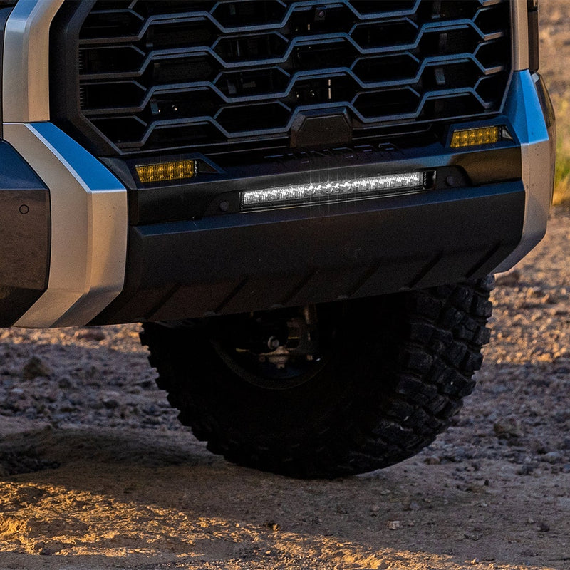 Rigid Selective Yellow SAE Fog Light Kit installed on a Toyota Tundra: low front view of a Toyota Tundra bumper with amber fog lights and a white light bar lit at dusk