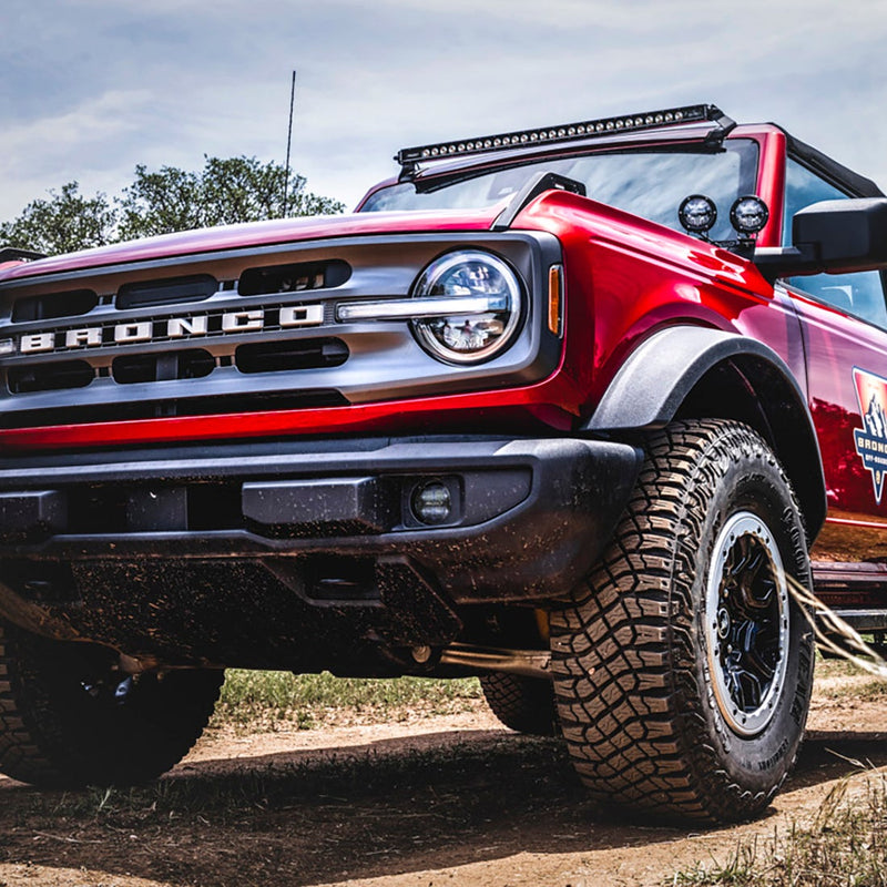 Rigid Standard Bumper 360-Series Fog Light Kit installed on a Ford Bronco: low angle of a red Ford Bronco front corner with BRONCO grille lettering and a round fog light in the bumper