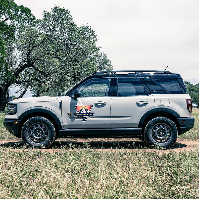 Rigid: Side profile of a white Ford Bronco Sport on a dirt track with small pods barely visible on the roof rack