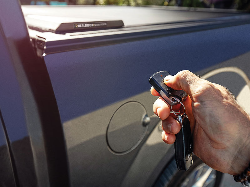 A hand working the Roll-N-Lock E-Series key fob beside the closed cover and its rail