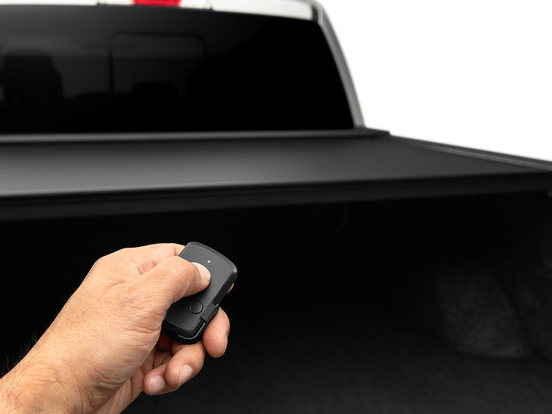 A hand pressing the Roll-N-Lock E-Series two-button wireless key fob with the powered cover closed behind it