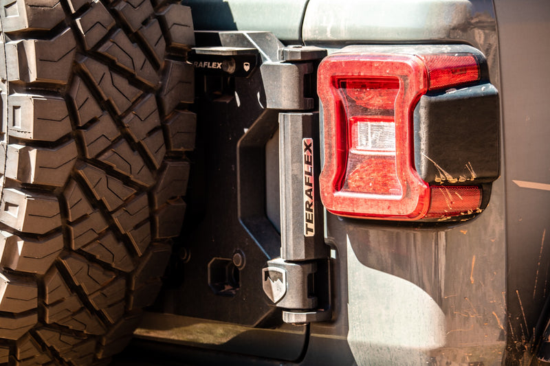 Close-up of the TeraFlex Tire Carrier & Tailgate Accessory: close-up of installed TeraFlex tailgate hinge next to Jeep Wrangler JL taillight and spare tire