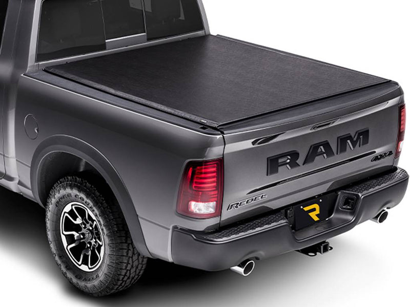 Black soft folding tonneau cover closed over the bed, rear three-quarter view on a white background