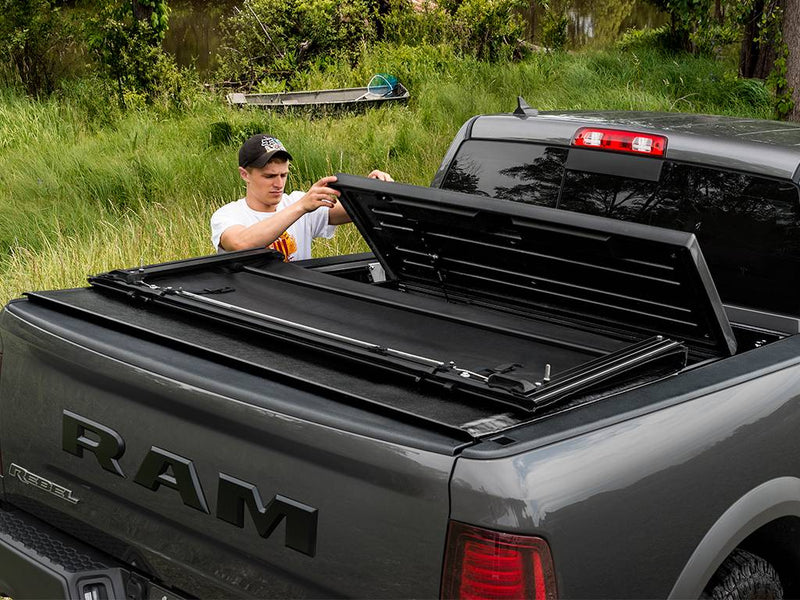 Man lifting the front hard section of the tonneau cover beside a grassy lake shore