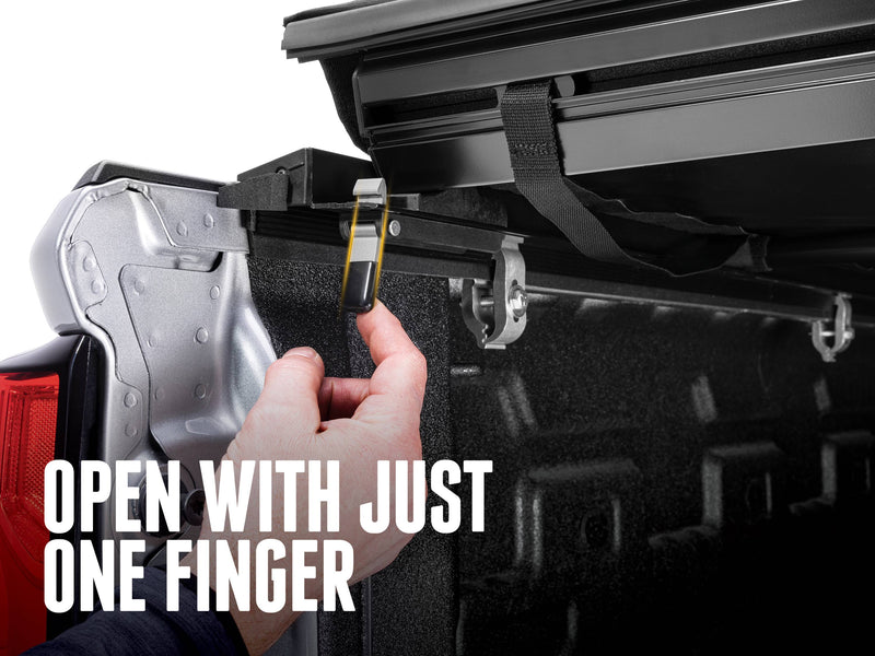 Hand pulling the quick-release latch strap at the tailgate end, text reads Open with just one finger