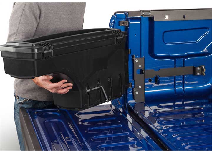 Two hands lifting the UnderCover SwingCase toolbox clear of its hinge pins, showing that the case comes out of the bed without tools