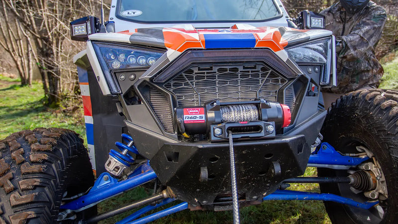 Warn R60-S powersports winch mounted on a sport side-by-side in open grassland, synthetic rope spooled on the drum