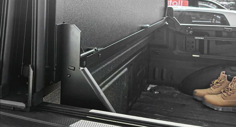 Worksport NEXUS hard folding tonneau cover on a pickup: inside-bed view of the flipped-up front panel held by the black auto-locking arm, with boots on the bed floor