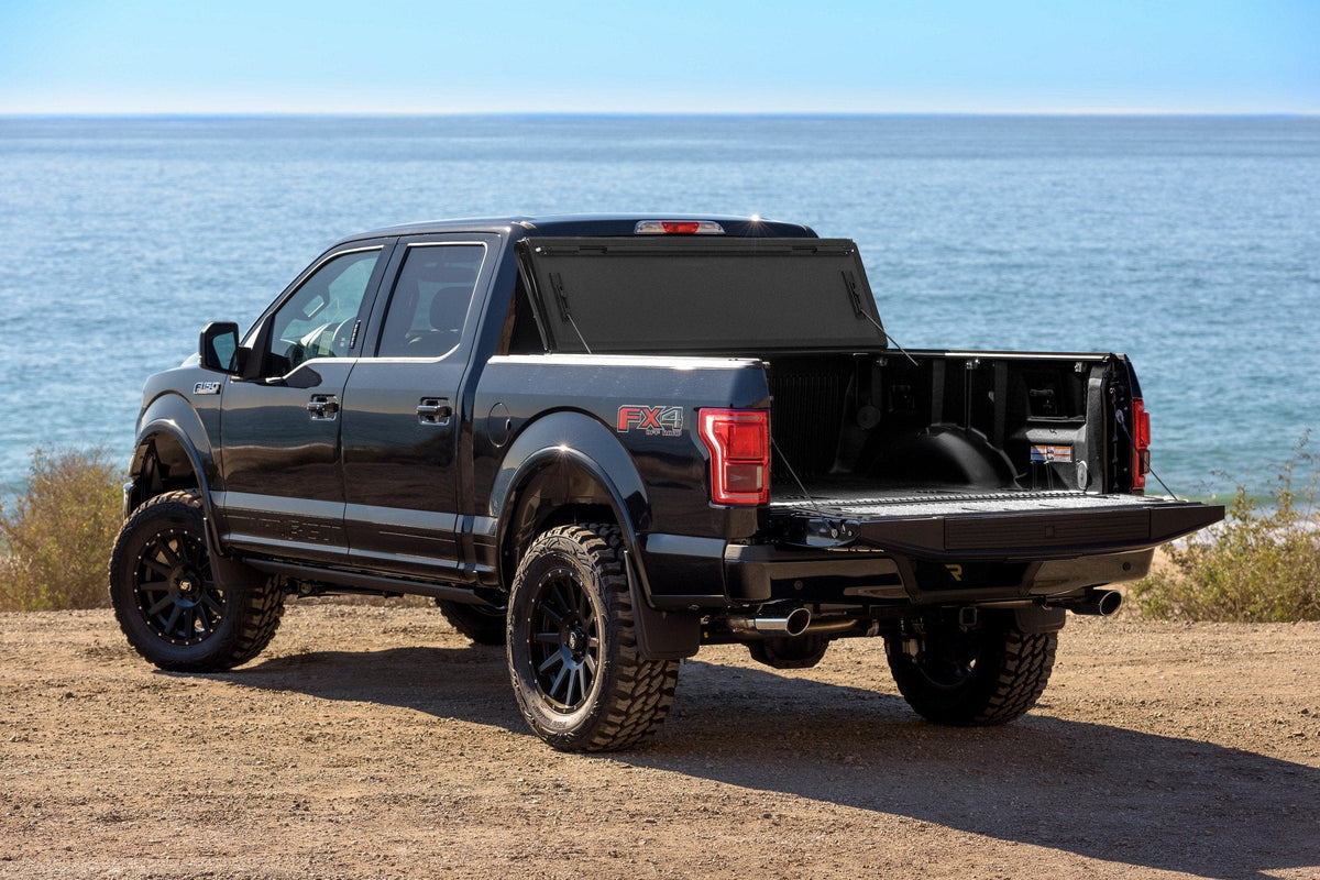 Black Ford F-150 at a beach with a BAKFlip MX4 hard folding cover folded up at the cab