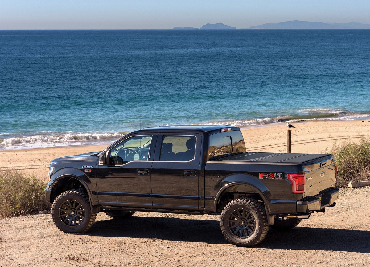 Blue 2016 Ford F-150 with a BAKFlip MX4 hard folding cover, parked on a beach
