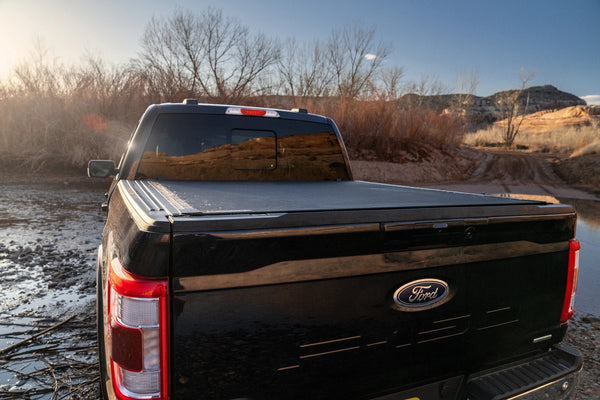 BAK Revolver X4s hard roll-up cover on a black 2021 Ford F-150 beside muddy water