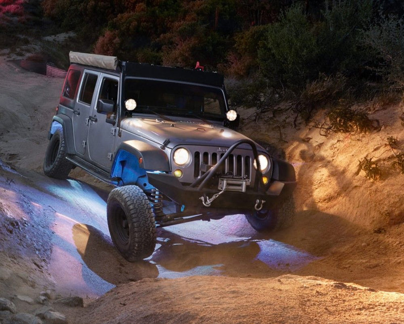 KC HiLiTES C-RGB Multi-Color Rock Light Kit, installed under a Jeep Wrangler lit white at night on the trail