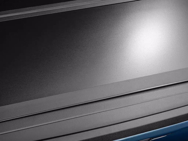 Raking-light close-up across the Select cover's matte-black textured panel surface and panel seam.