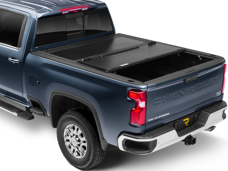 UnderCover Flex hard folding tonneau cover part-open with the rear panel folded forward over the middle panel, rear three-quarter view, textured gloss-black panels.