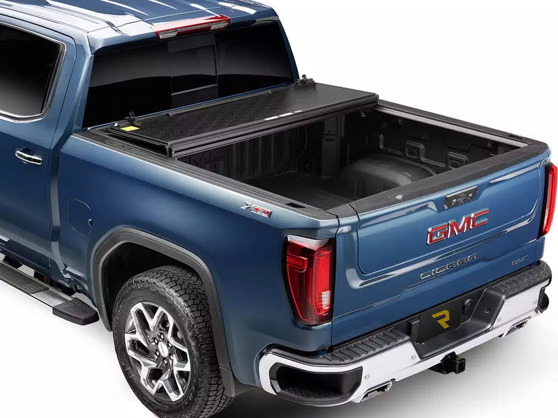 UnderCover Select hard folding tonneau cover folded open and stacked at the bulkhead with most of the bed exposed, rear three-quarter view.
