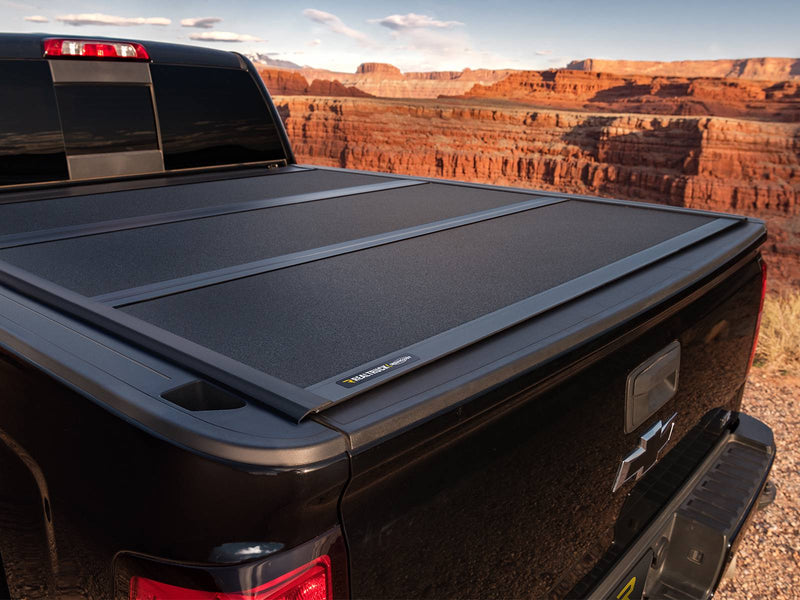 UnderCover ArmorFlex hard folding tonneau cover closed and flush on a pickup bed at a canyon overlook, tight rear three-quarter view showing the panel seams and rear bed rail.