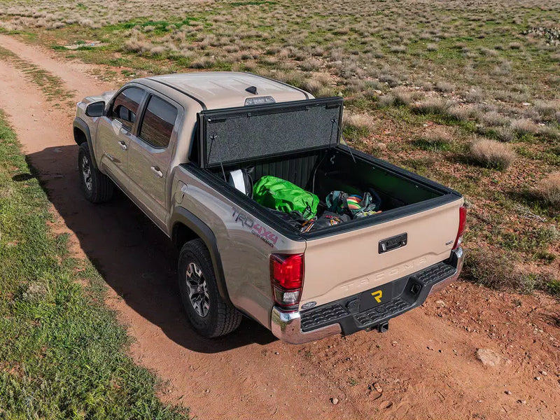UnderCover Ultra Flex hard folding tonneau cover folded open at the bulkhead with the bed loaded with gear, real-world scene on a grassland track.