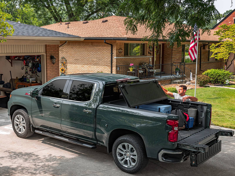 UnderCover Select part-open with the tailgate down, wide driveway scene showing the full bed