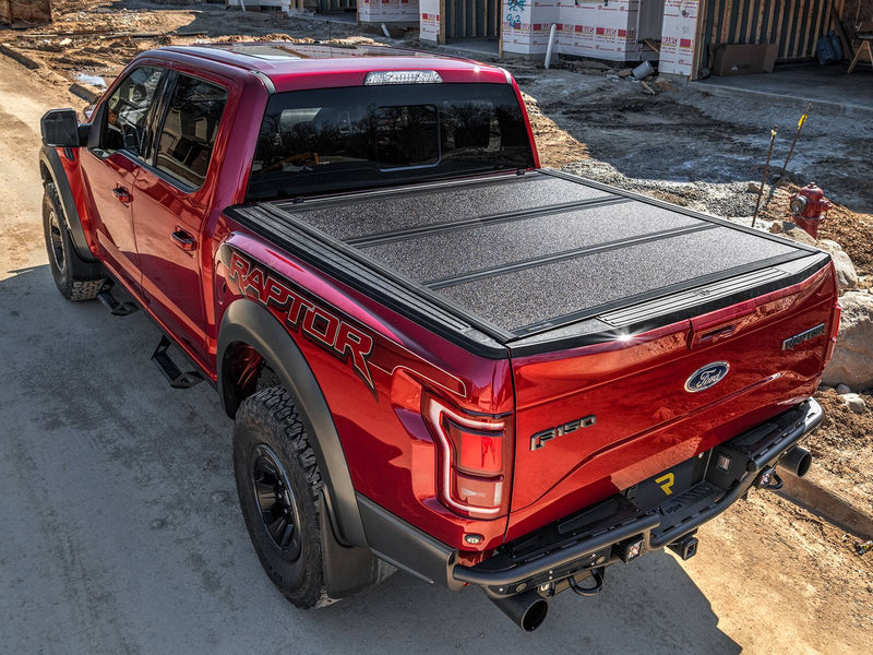 UnderCover ArmorFlex hard folding tonneau cover closed on a pickup bed at a construction site, high rear three-quarter view showing the full textured panel surface.