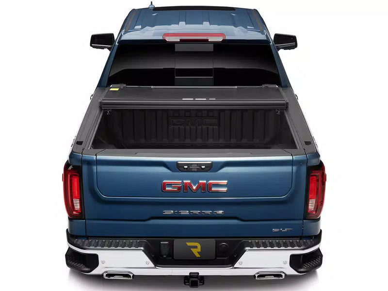 UnderCover Select hard folding tonneau cover folded open and stacked against the bulkhead, straight rear view into the bed on a 2019-2026 GMC Sierra 1500.