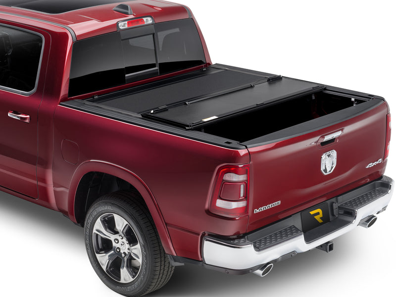 UnderCover ArmorFlex hard folding tonneau cover part-open, rear panel folded forward over the middle panel with a third of the bed exposed, rear three-quarter view on a 2019-2026 Ram 1500.