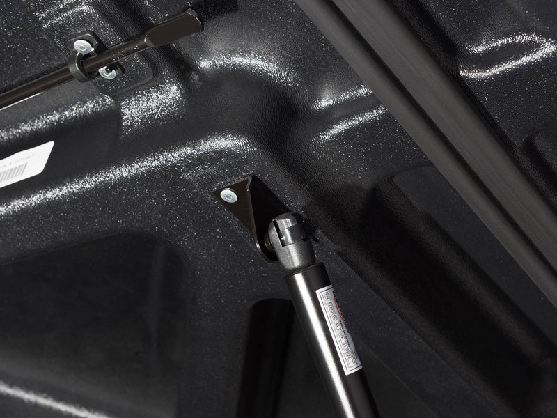 Close-up of the LUX lid underside showing the gas strut, the prop rod and the printed compliance labels.