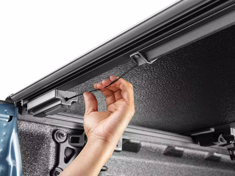 A hand routing the Select drain tube under the cover's side rail inside the bed.