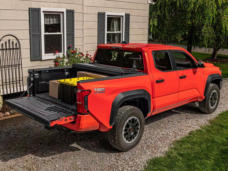 UnderCover Select hard folding tonneau cover folded forward with the tailgate down and the bed loaded with boxes, real-world driveway scene.