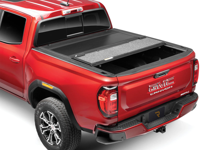 UnderCover Ultra Flex hard folding tonneau cover part-open on a pickup bed, rear panel folded forward onto the middle panel with its grey underside facing up and the rear third of the bed exposed, rear three-quarter view.